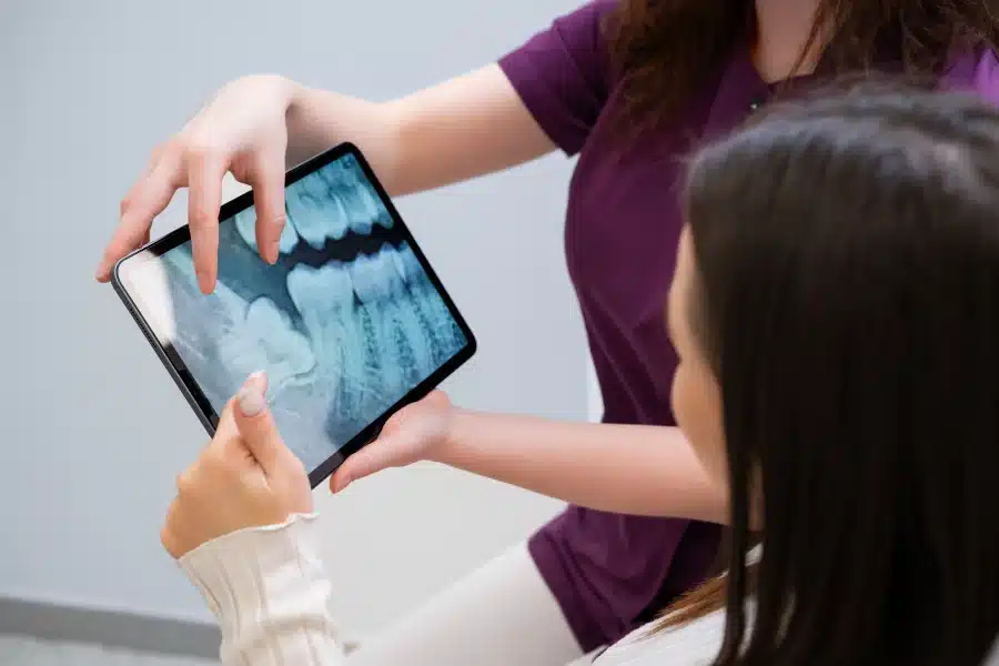 Dentist showing patient dental X-ray on tablet for wisdom teeth extractions